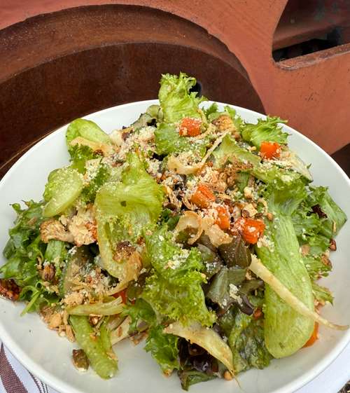 A salad of baby green leaf lettuce, with rosted carrots, and other seasonal vegetables sits in a white bowl